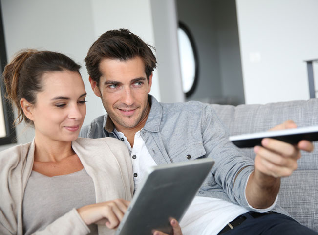 Muž přepíná programy na hlavní televizi v domácnosti. Žena sleduje své pořady na tabletu. Ilustrační foto Shutterstock.com